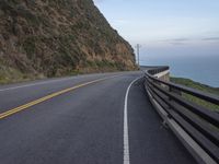 a curved road beside the ocean with rocky hills and a body of water in the background