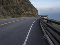 a curved road beside the ocean with rocky hills and a body of water in the background