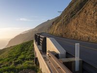 a highway with grass and shrubs along it on the hillside next to an ocean view