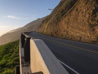 a highway with grass and shrubs along it on the hillside next to an ocean view