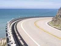 a highway near the coast with a road fence on each side and an ocean and hill in the background