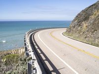 a highway near the coast with a road fence on each side and an ocean and hill in the background