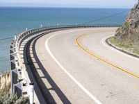 a highway near the coast with a road fence on each side and an ocean and hill in the background