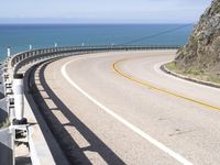 a highway near the coast with a road fence on each side and an ocean and hill in the background