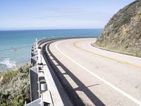 a highway near the coast with a road fence on each side and an ocean and hill in the background