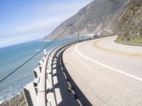 a highway near the coast with a road fence on each side and an ocean and hill in the background