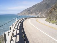 a highway near the coast with a road fence on each side and an ocean and hill in the background