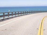 an open road stretching over water on a sunny day with mountains in the background along