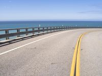 an open road stretching over water on a sunny day with mountains in the background along