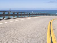 an open road stretching over water on a sunny day with mountains in the background along