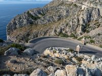 a road near the ocean in france with the ocean behind it and some hills in the distance