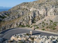 a road near the ocean in france with the ocean behind it and some hills in the distance