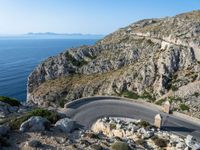 a road near the ocean in france with the ocean behind it and some hills in the distance