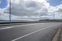 a deserted highway passes past a body of water and on the far side, it is a sky with clouds