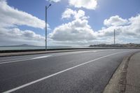 a deserted highway passes past a body of water and on the far side, it is a sky with clouds