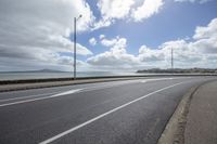 a deserted highway passes past a body of water and on the far side, it is a sky with clouds