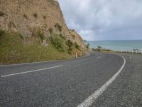 a motorcycle is parked on a highway beside the ocean in front of a cliff wall