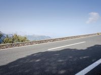 a side view of a long straight road, leading away from a bush next to a mountain