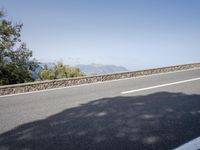 a side view of a long straight road, leading away from a bush next to a mountain