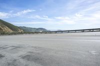 an empty highway with a mountain in the background and a long bridge spanning between it