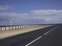 an empty road near a sandy shore in front of some water and sand with a few white clouds above