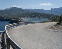 a curve on a highway near the ocean with mountains behind it and people walking by