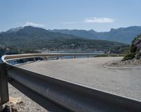 a curve on a highway near the ocean with mountains behind it and people walking by