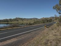 a highway with some white lines and grass on both sides and the water in the background