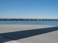 the shadow is cast on the asphalt near a large body of water and a bridge