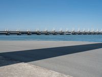 the shadow is cast on the asphalt near a large body of water and a bridge