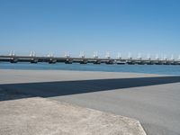 the shadow is cast on the asphalt near a large body of water and a bridge