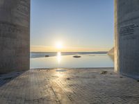 a sun shines behind two stone pillars overlooking a bay and a blue sky that has water