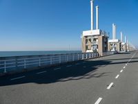 a bridge over the ocean with construction equipment in the background and two people walking on it