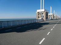 a bridge over the ocean with construction equipment in the background and two people walking on it