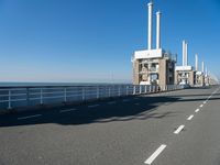 a bridge over the ocean with construction equipment in the background and two people walking on it