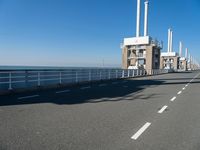 a bridge over the ocean with construction equipment in the background and two people walking on it