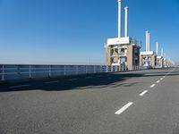 a bridge over the ocean with construction equipment in the background and two people walking on it