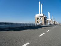 a bridge over the ocean with construction equipment in the background and two people walking on it