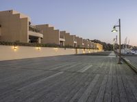 the wooden boardwalk leading down to the water in front of a hotel complex with light posts on either side