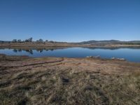 a large body of water with some grass and hills in the background by a small lake