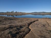 a large body of water with some grass and hills in the background by a small lake