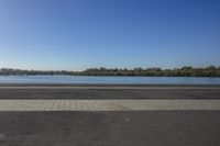 empty paved road with benches beside the edge and a large body of water in the distance