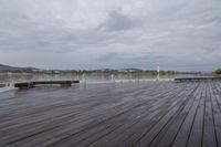 a wooden deck by a lake under a cloudy sky with benches nearby and water in the background