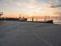 a man on a skateboard rides down the street by a pier at sunset in this photo