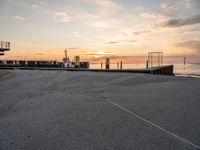 a man on a skateboard rides down the street by a pier at sunset in this photo