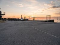 a man on a skateboard rides down the street by a pier at sunset in this photo