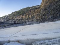 a skateboard is propped up against the cement on a rocky beach near a cliff