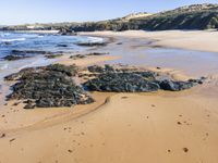 a person stands near a rocky shoreline in the water on the sand and waves rolls in