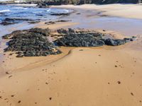 a person stands near a rocky shoreline in the water on the sand and waves rolls in