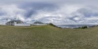 two white buildings standing on a green hillside near the ocean with clouds overhead and blue sky